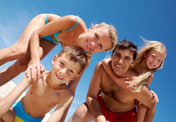 Famille souriante avec enfants en maillot sur la plage regardant l'objectif 