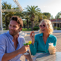 couple homme et femme avec une boisson souriant devant la piscine du camping Marvilla Parks